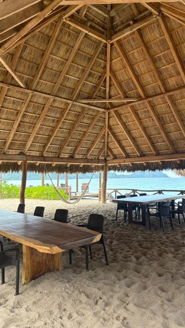 Mesas y hamaca bajo la palapa frente al mar